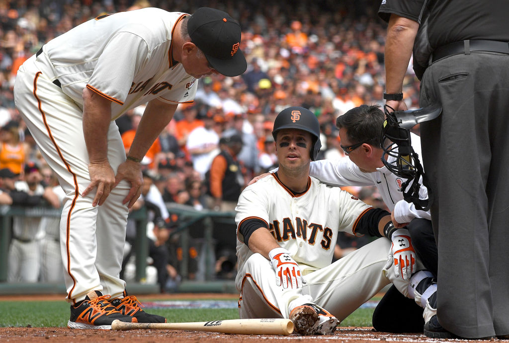 SAN FRANCISCO, CA - APRIL 10: Buster Posey #28 of the San Francisco Giants sits on the ground and is checked on by manger Bruce Bochy #15 and trainer Dave Groeschner after Posey was hit in the head with a pitch in the bottom of the first inning at AT&T Park on April 10, 2017 in San Francisco, California. Posey was taken out of the game after he was hit by the pitch.