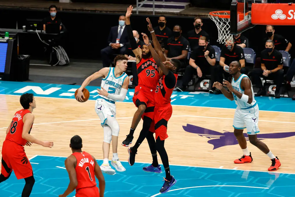 CHARLOTTE, NORTH CAROLINA - DECEMBER 12: LaMelo Ball #2 of the Charlotte Hornets looks to pass against DeAndre' Bembry #95 and Chris Boucher #25 of the Toronto Raptors during the second half of their game at Spectrum Center on December 12, 2020 in Charlotte, North Carolina. (Photo by Jared C. Tilton/Getty Images)