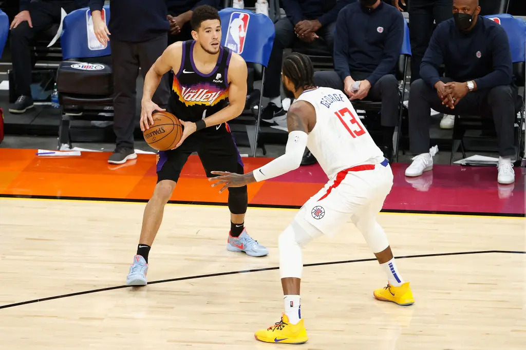 PHOENIX, ARIZONA - APRIL 28: Devin Booker #1 of the Phoenix Suns handles the ball against Paul George #13 of the LA Clippers during the NBA game at Phoenix Suns Arena on April 28, 2021 in Phoenix, Arizona. The Suns defeated the Clippers 109-101