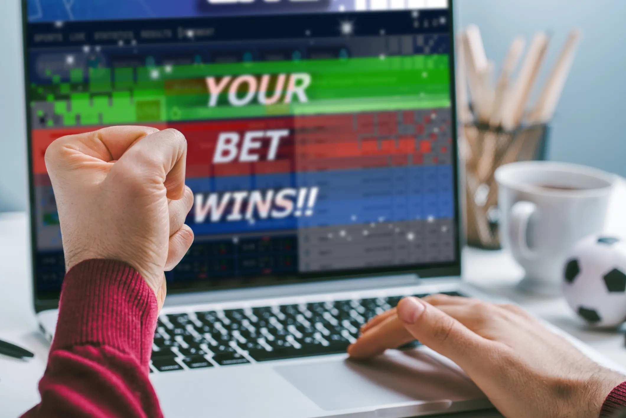 Cropped shot close up of male fist clenched with triumph in front of laptop screen. Man celebrating money win at bookmaker's website, his bet played.